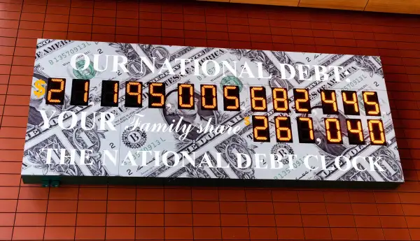 The National Debt Clock is a very large digital display of the current gross national debt of the United States. It is mounted on a western facing wall in a wide covered alley in the middle of the block and runs between West 42nd Street and West 43rd Street. The alley is located between Sixth Avenue and Broadway in New York City. The displayed debt shown, over 21 trillion dollars, is as of July 13, 2018 when this image was created.