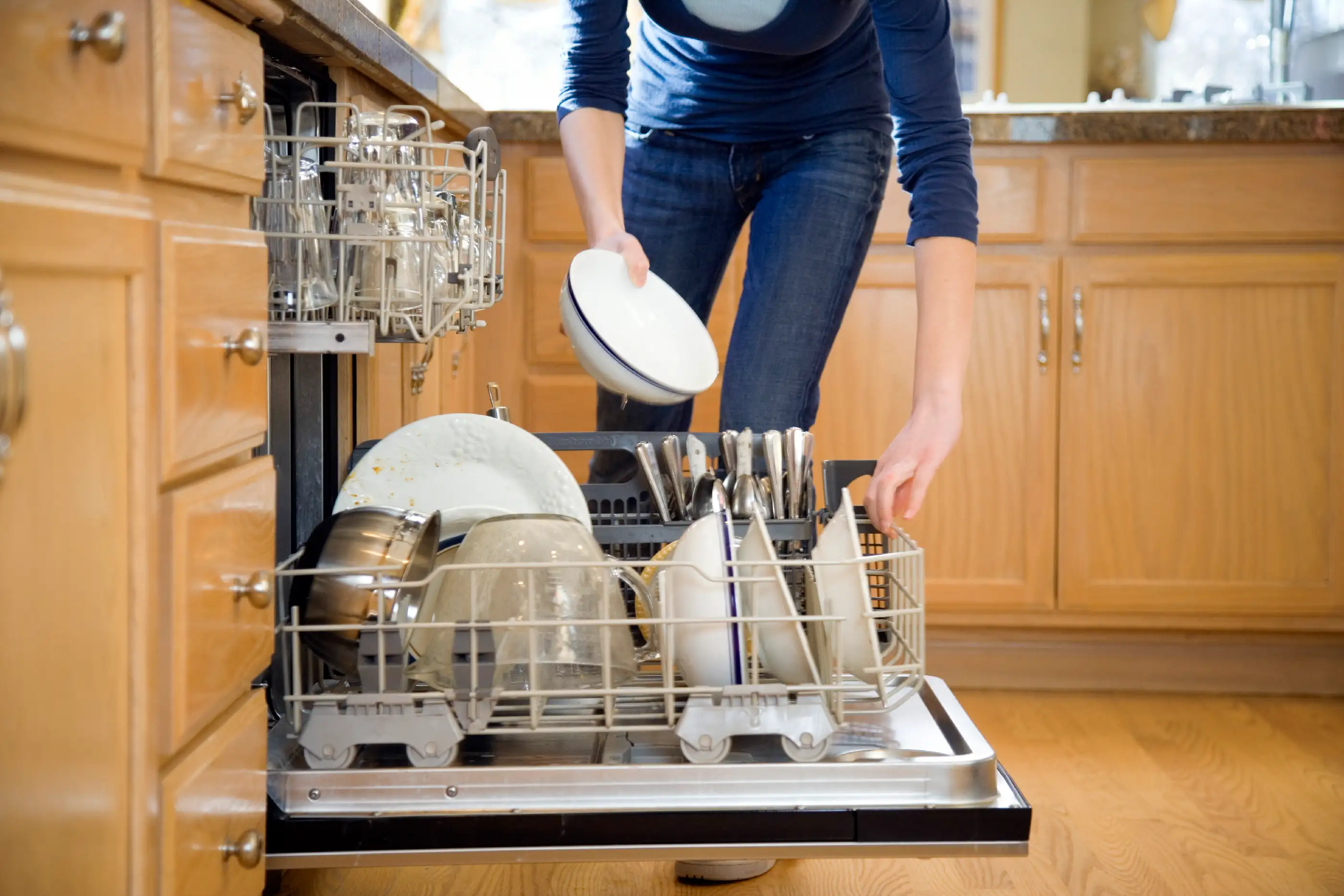 Teenage girl (16-18) putting dishes in dishwasher, low section