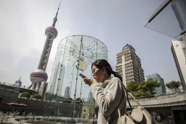 A woman using a smartphone walks past an Apple Inc. store in Shanghai.