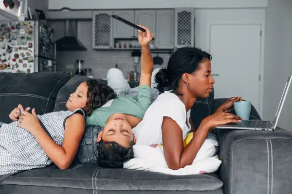 Mother and two kids sitting on the sofa at home using digital devices.