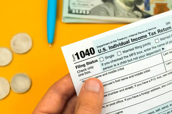 Accountant filling out US tax forms 1040 with some money in the background