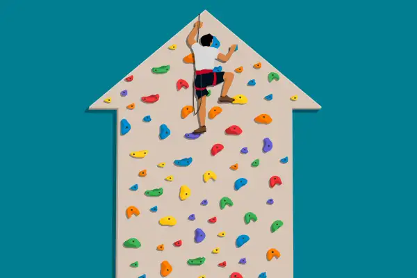 A person climbing to the  peak  of a climbing wall shaped like an upward trending arrow, with no where to go but down