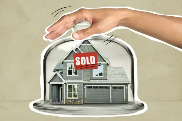 House with a sold sign inside a glass cake-stand with a hand holding down the lid