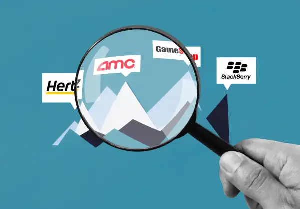 A hand holding a magnifying glass inspecting AMC, Hertz, GameStop and BlackBerry Stocks