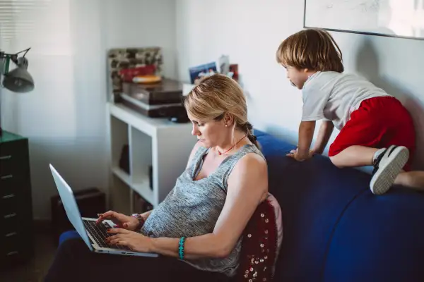 Young pregnant woman working on her computer while older child plays at her side
