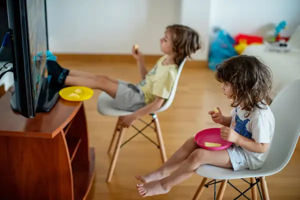 Two kids eating fruit while watching television