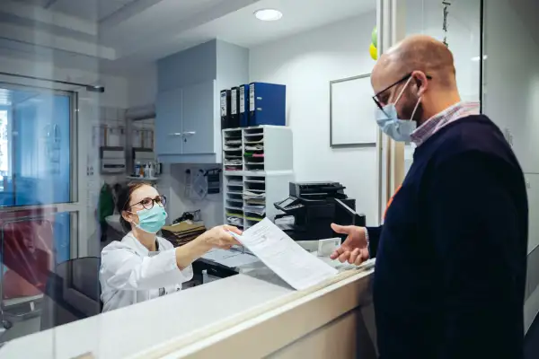 Employee at reception desk of hospital handing over a medical form to a visitor