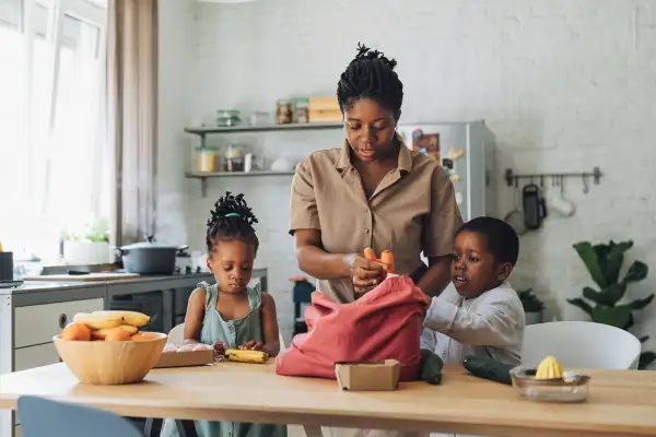 Mother, daughter and son preparing vegetables for lunch at a wooden kitchen table