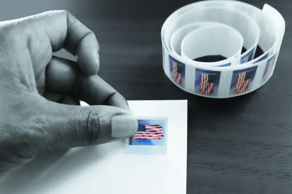 Close-up of a hand placing a stamp with the United States flag on a white envelope.