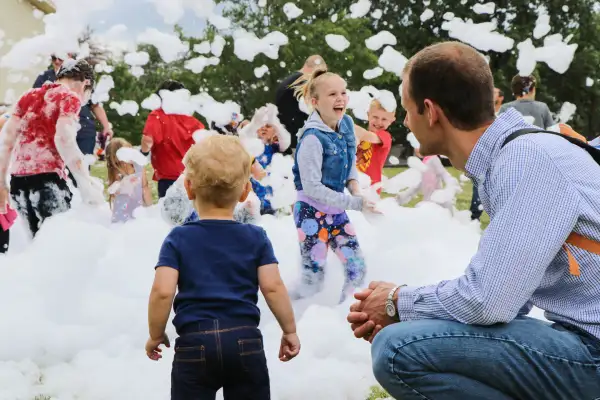 Dad and son with girl in background with bubbles at party in the park in Urbandale Iowa