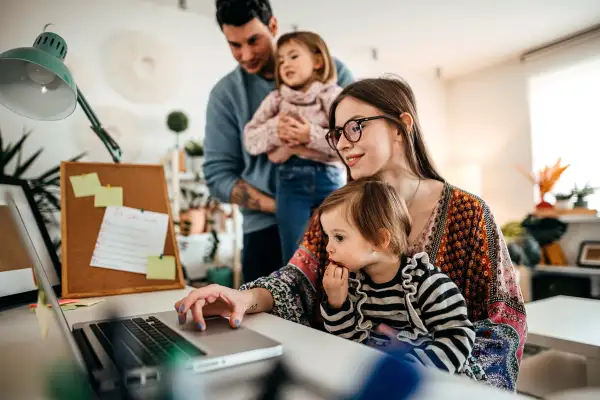 A couple with two young daughters look at something on a laptop