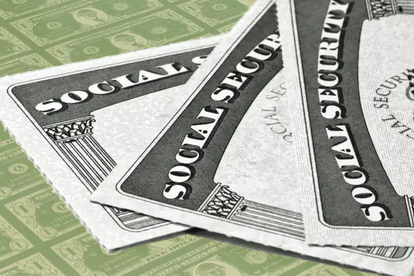 Close-up of three Social Security Cards stacked on top of each other, with one dollar bills in the background