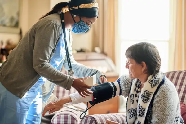 Young nurse wearing a protective face mask taking a senior patient's blood pressure