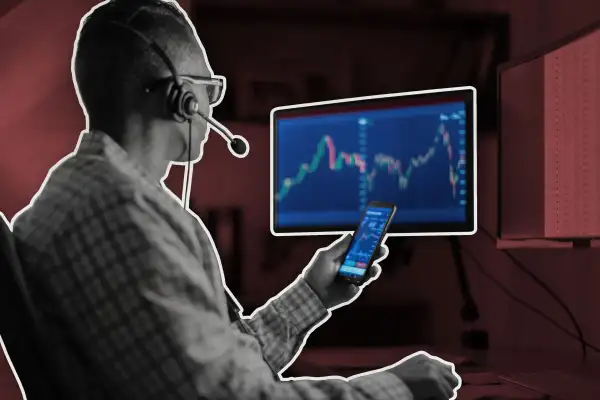 Man Holding Smart Phone While Staring At A Computer Screen Displaying Stock Market Graphics