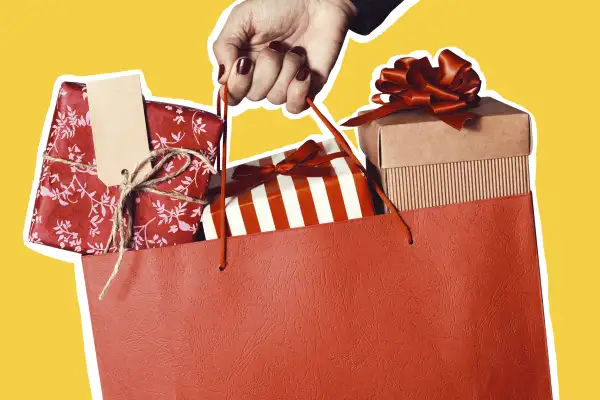 Closeup of a hand holding a bag with multiple gifts inside wrapped in holiday themed paper