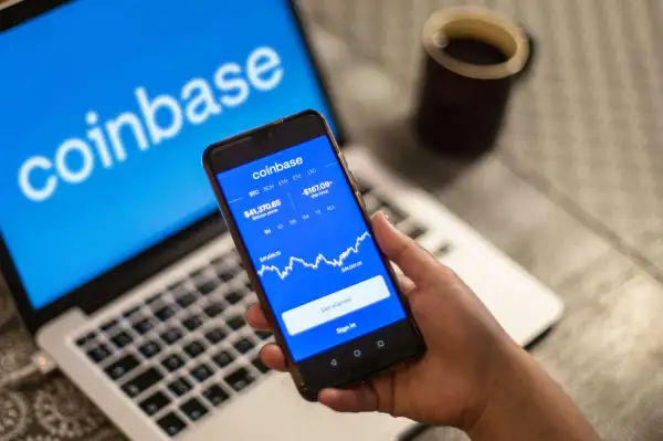 Coinbase logo is seen displayed on a smartphone and a laptop in the background