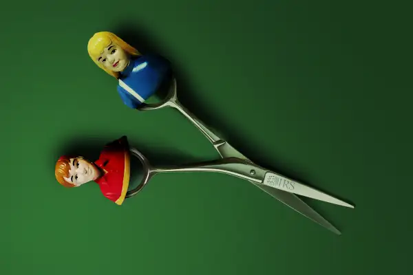 Photo-Illustration of a pair of scissors with the IRS logo, where one side of has a toy figure of a girl and the other a toy figure of a boy