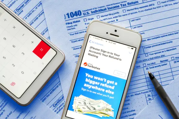 Close-up of a smartphone with the Turbo Tax App open and a 1040 Tax Form in the background