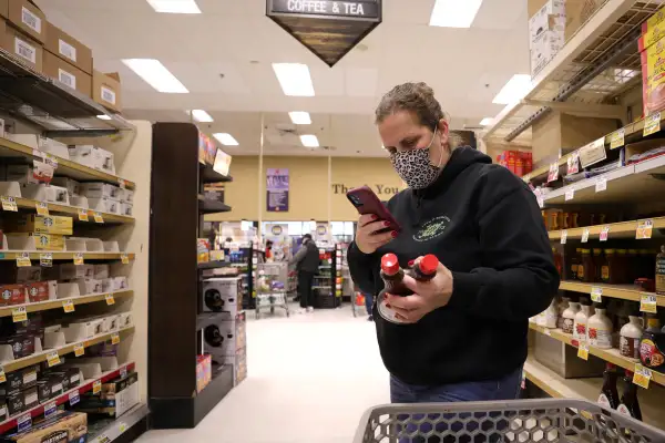 Woman compares prices of maple syrup at a grocery store before buying them