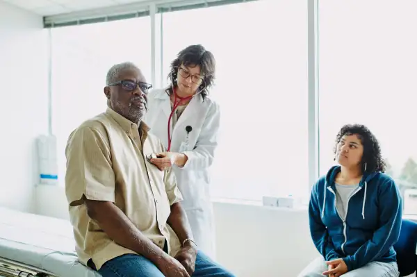 Female doctor using stethoscope to listen to senior male patients breathing during medical exam