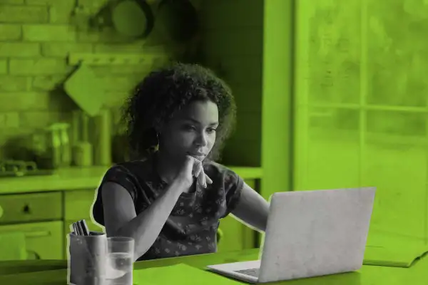 Woman Sitting Down At Kitchen Table Looking At Laptop