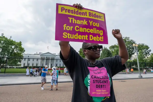 Woman with a sign in front of the White House that reads  President Biden: Thank you for canceling student debt!