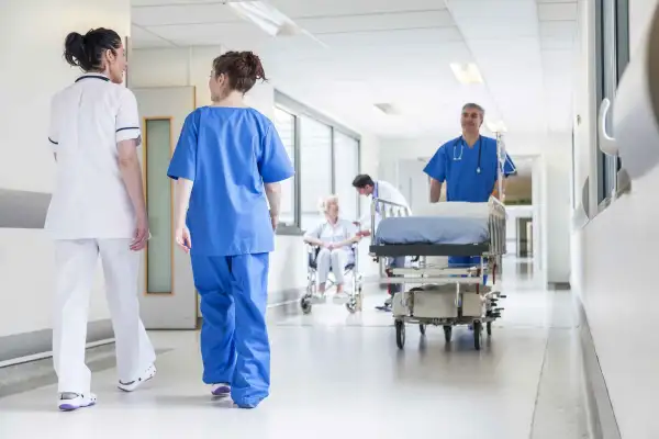 nurse pushing stretcher gurney bed in hospital corridor with doctors & senior female patient