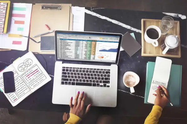 Top view of a person using laptop surrounded by spreadsheets