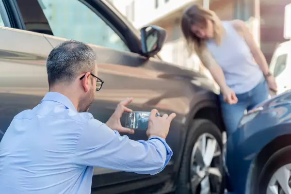 Man taking a picture with his phone of his car damage after an accident