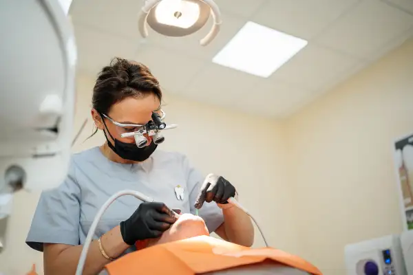 female dentist in binocular glasses treats a tooth to a patient man