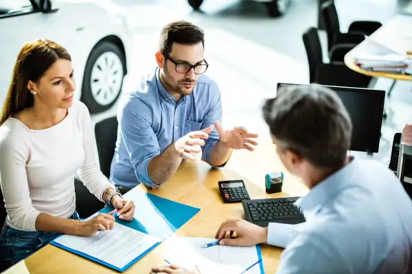 Couple talking to salesperson on a meeting in a car showroom.