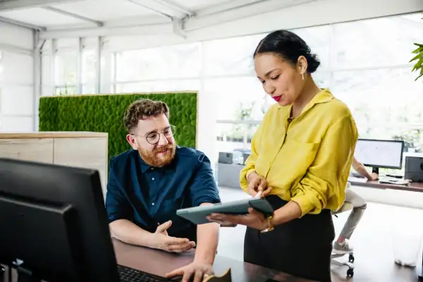 An office manager showing some documents on a digital tablet to her colleague in a bright, modern office space