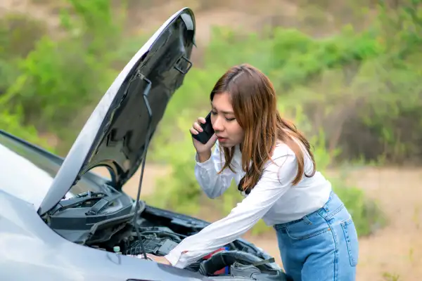 Woman talking on her phone while inspecting something under the hood of her car
