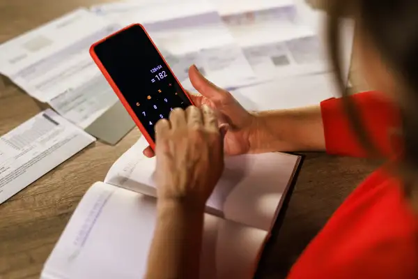 Close-up of a person using a calculator lookin over bills