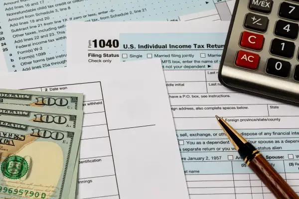 Tax forms, pen, dollar bills, and calculator