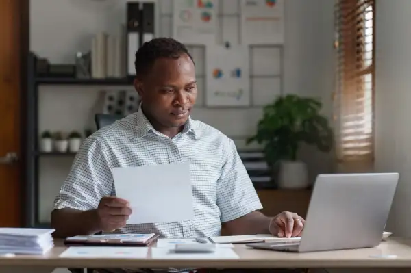 Man using his laptop while looking over papers