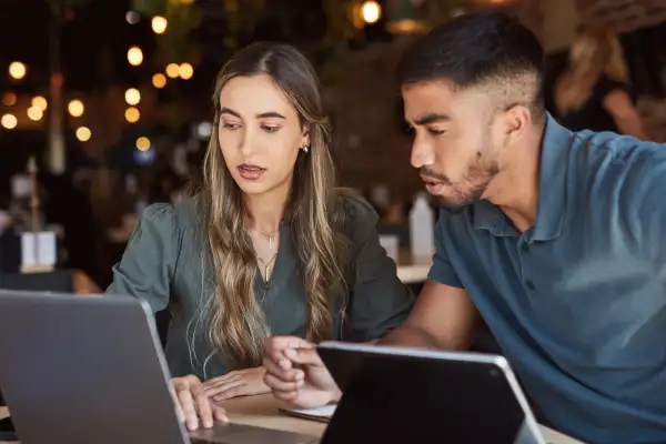 A man an a woman sitting at a desk looking at a laptop screen