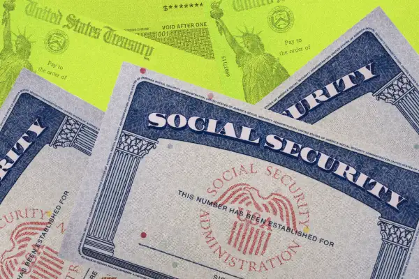 Photo collage of multiple social security cards stacked on top of each other and stimulus checks in the background