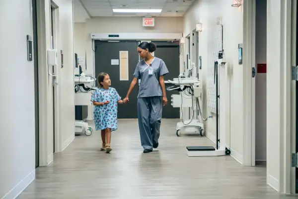 Nurse walking a young patient by the hand in a hospital hallway