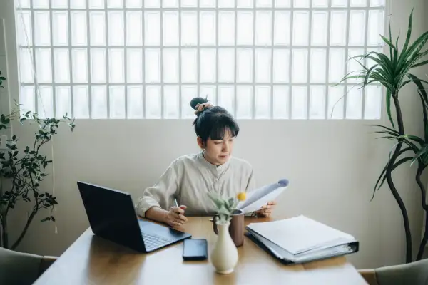 Woman at home looking over some documents and using a laptop