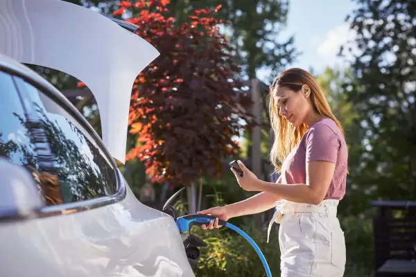 Woman looking at her phone while she is charging her white EV car