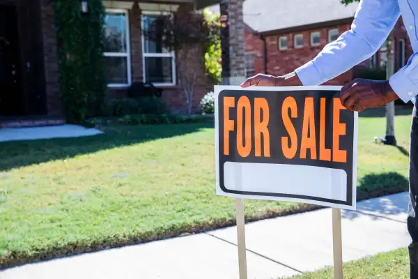 Person sets up  For Sale  sign outside a house