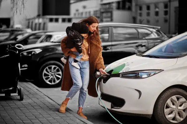 Young mother with child charging electro car at the electric gas station.