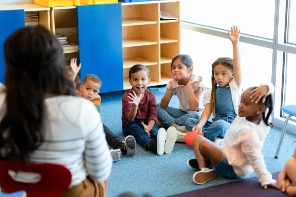 Preschool age children sit in a circle on the floor of a classroom