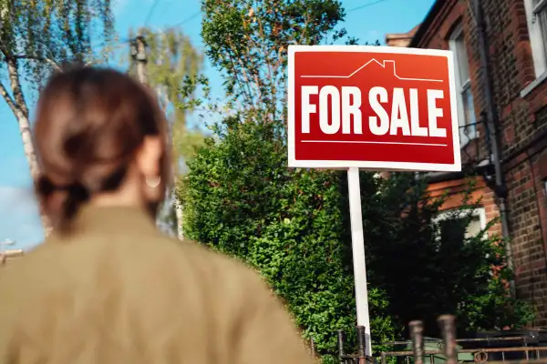 Photo of a person looking at a house's sale sign