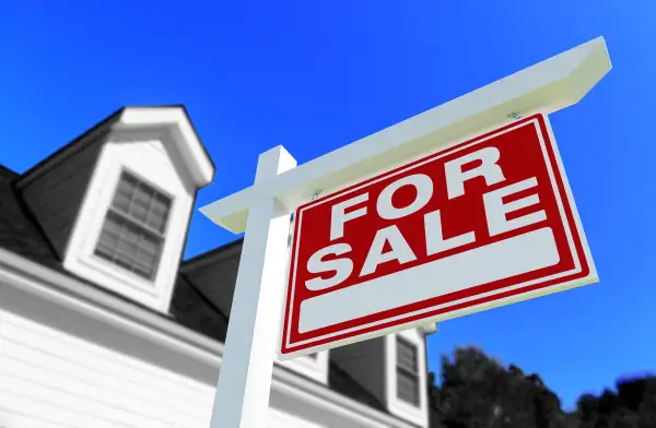 Close-up of a for sale sign in-front of a suburban home