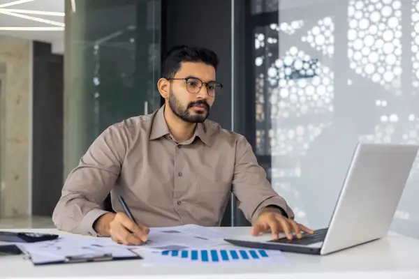 Man in an office working using his laptop and looking over business papers