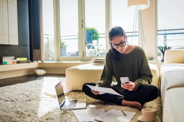 Young woman sitting on the floor of her living room looking over bills