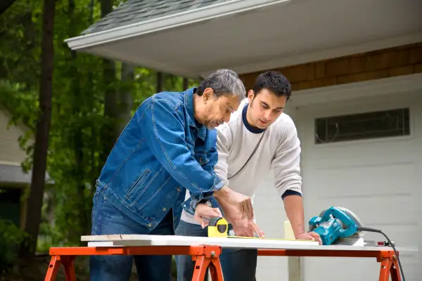 Two men cutting wood outside of a house for a home renovation