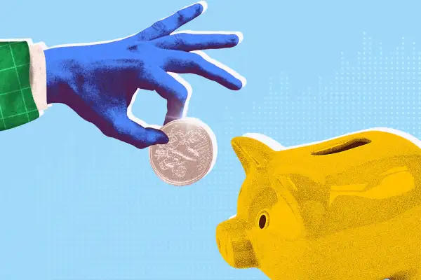 A hand dropping a coin into a piggy bank.